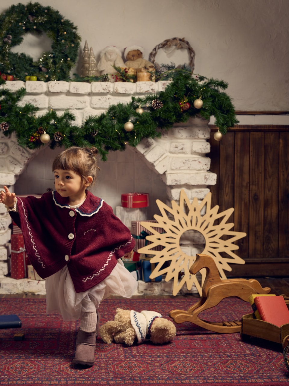 赤い襟付きのポンチョをきた子供が暖炉の前で駆け出している画像
