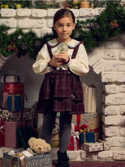 サスペンダー付きのスカートを着た子供が正面を向いている画像